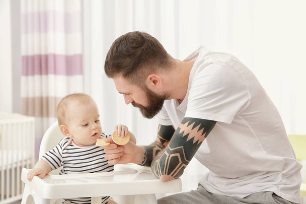 Handsome tattooed young man feeding cute little baby at home - Zdjęcie, obraz