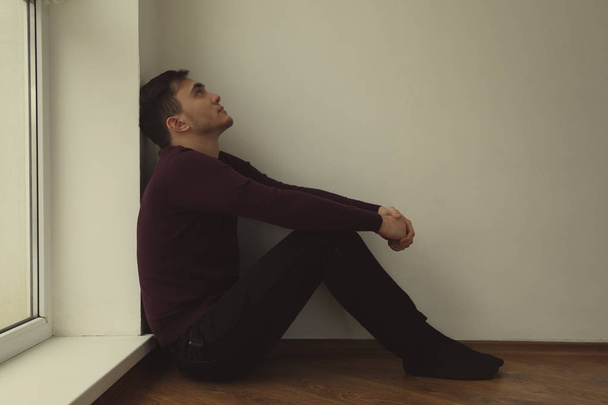 Handsome depressed man sitting on floor at home - 写真・画像