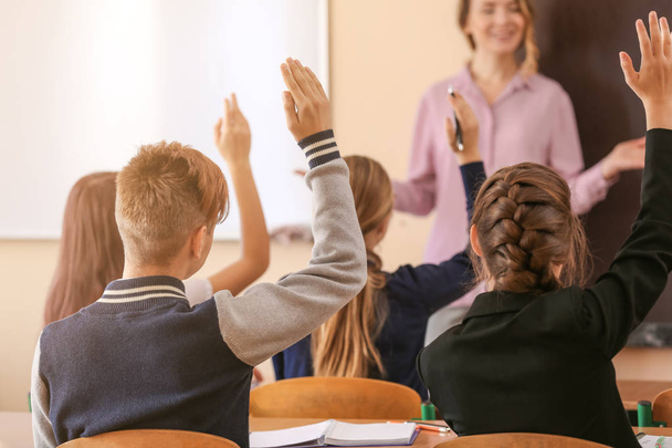 Alumnos escuchando al maestro y levantando las manos para responder en el aula
 - Foto, Imagen