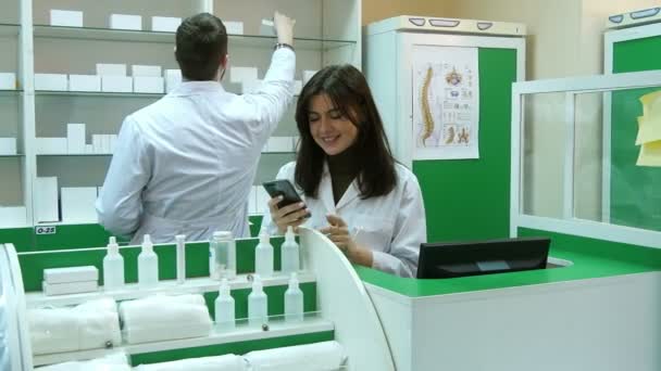 Женщина-фармацевт позитивно реагирует с помощью смартфона, разговаривает со своим коллегой
 - Кадры, видео