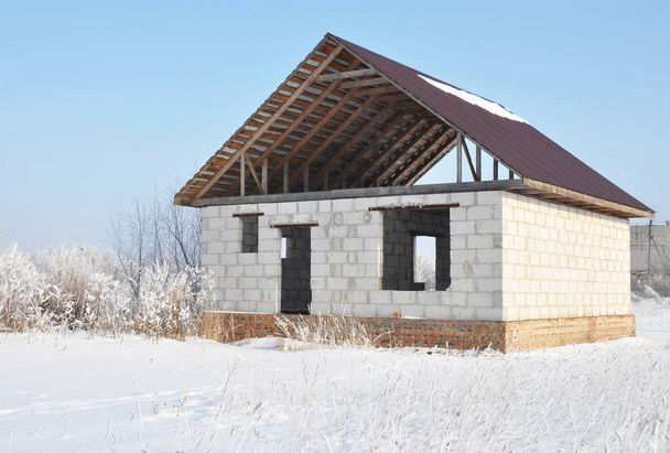 Befejezetlen otthon tetőfedő fém csempe építése. Tetőszerkezet építése télen. Téli otthon épület.  - Fotó, kép
