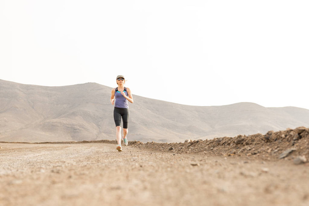 背景の山の未舗装の道路上にジョギングの女性に合う - 写真・画像