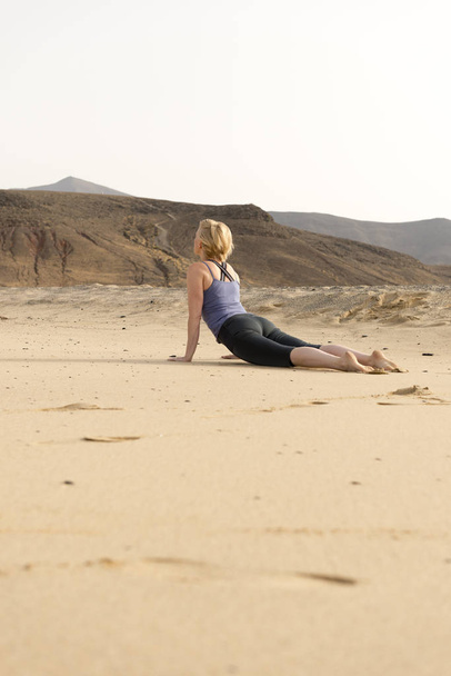 Donna in forma che fa Cobra Yoga Posa nella sabbia esterna
 - Foto, immagini