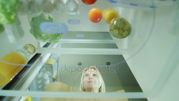 Una giovane donna carica il cibo in frigo. Apre la porta del frigorifero e ci mette appena comprato verdure. Vista interna
 - Filmati, video