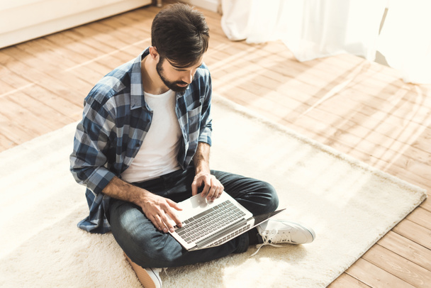 Человек сидит на ковре и печатает на ноутбуке
 - Фото, изображение