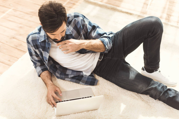 hombre acostado en la alfombra y el uso de ordenador portátil
 - Foto, imagen
