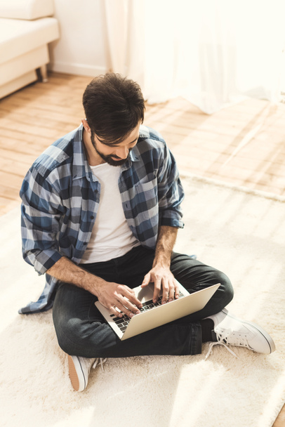 Homem sentado no tapete e digitando no laptop
 - Foto, Imagem
