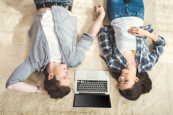 pareja acostada en la alfombra entre el ordenador portátil
 - Foto, Imagen