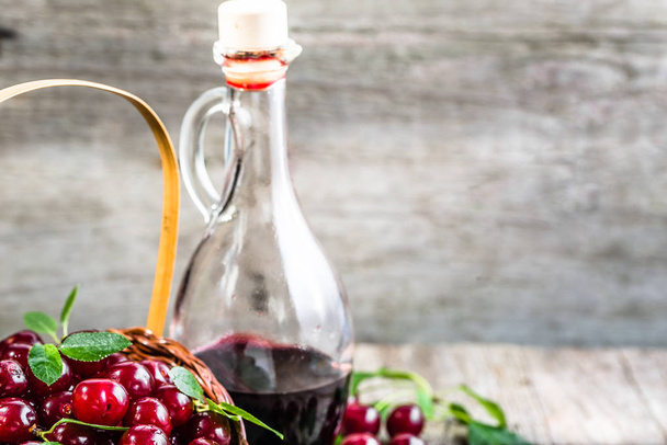 Cherry wine in a glass bottle on wooden table. Sweet alcohol made from cherry fruits - Foto, imagen