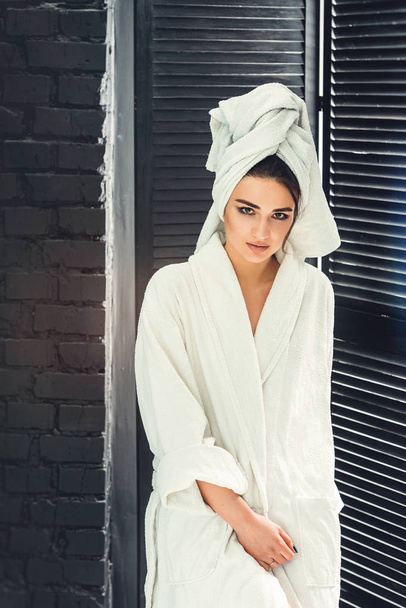 sexy young girl with dark hair, big eyes and dark eyebrows wearing white bath robe whith towel on her head. - Photo, Image