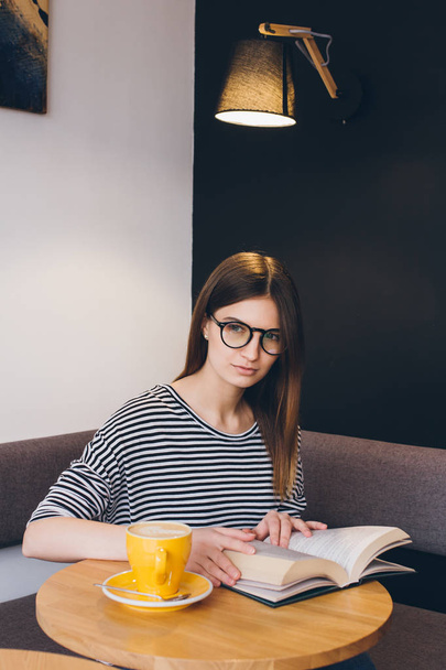 Mädchen mit Brille liest in einem Café ein Buch - Foto, Bild