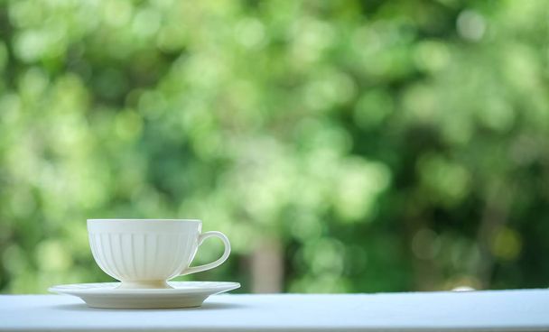 Біла чашка кави на столі з зеленим розмитим фоном
. - Фото, зображення
