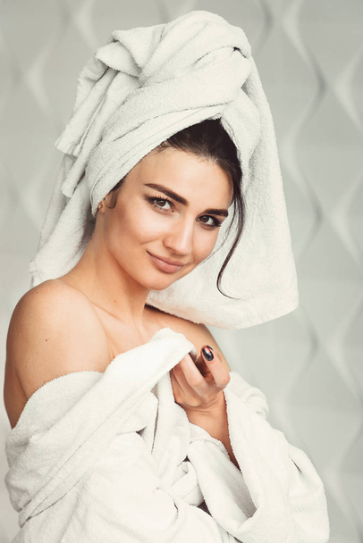 sexy jonge meisje met donker haar, grote ogen en donkere wenkbrauwen, het dragen van witte robe whith badhanddoek op haar hoofd. - Foto, afbeelding