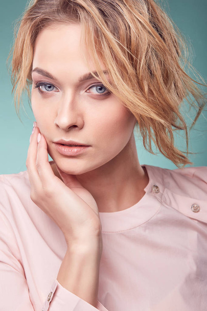 Closeup portrait of young serious romantic blonde woman with big eyes and wavy hair, wearing light pink dress in studio with turquoise background - Foto, afbeelding