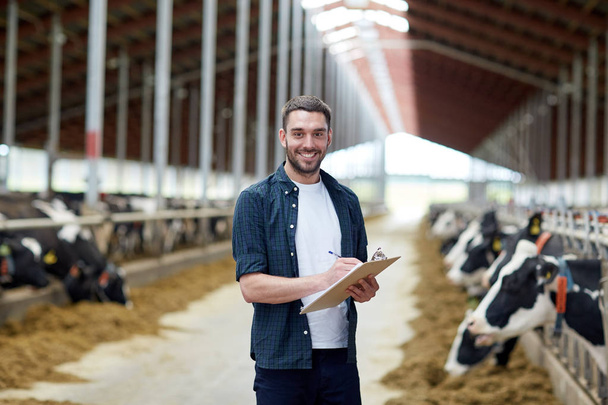 farmer with clipboard and cows in cowshed on farm - Photo, image