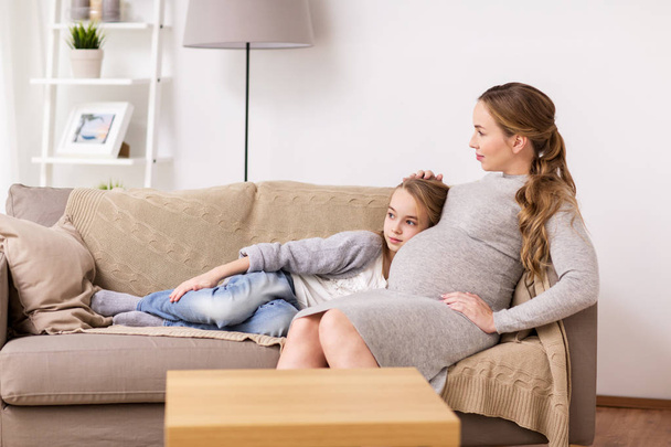 happy pregnant woman and girl on sofa at home - Foto, Imagem