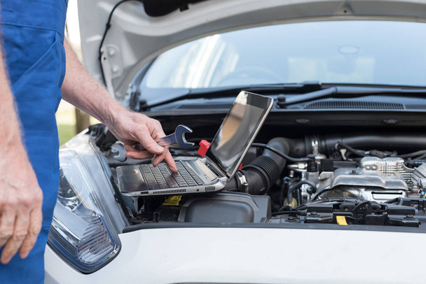 Mechanic using laptop for checking car engine - Foto, afbeelding