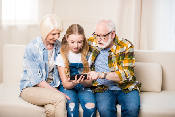 Girl with grandparents using smartphone - Foto, Imagen