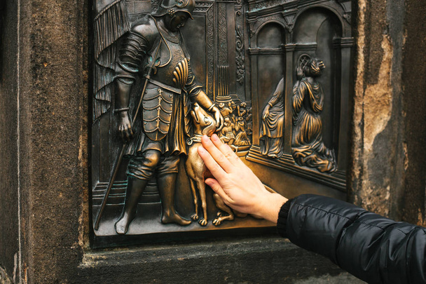 Nainen turisti koskettaa pronssi patsas John Nepomuk Kaarlen sillalla onnea. Legendoja. Praha, Tsekin tasavalta
 - Valokuva, kuva