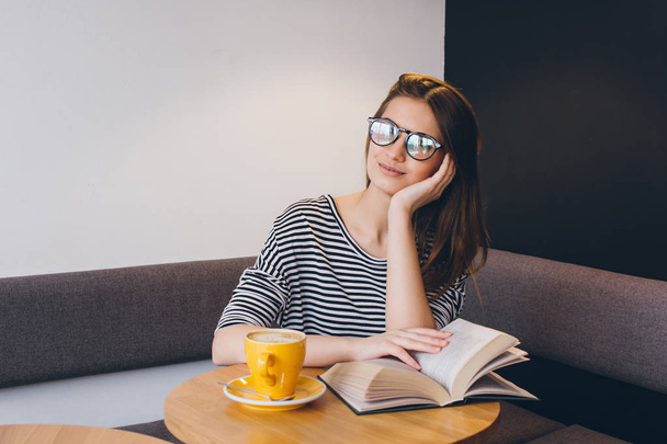 Girl in glasses reading a book in a coffee shop - Foto, imagen
