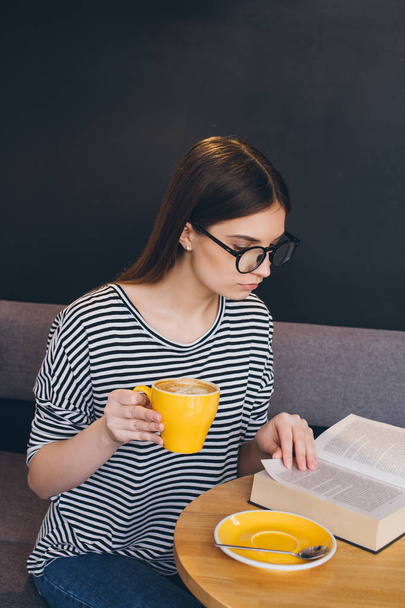 Girl in glasses reading a book in a coffee shop - 写真・画像