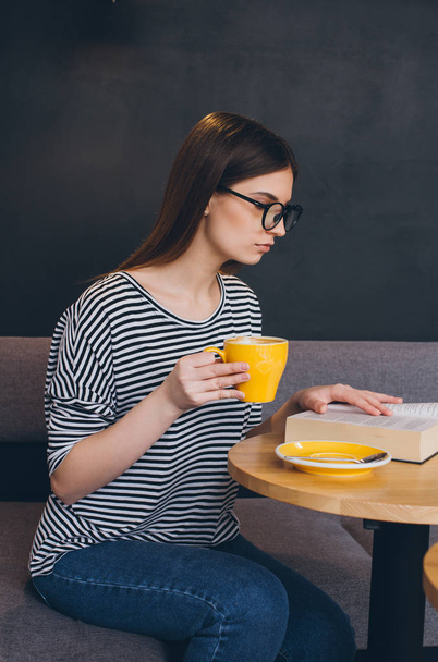 Girl in glasses reading a book in a coffee shop - Fotoğraf, Görsel