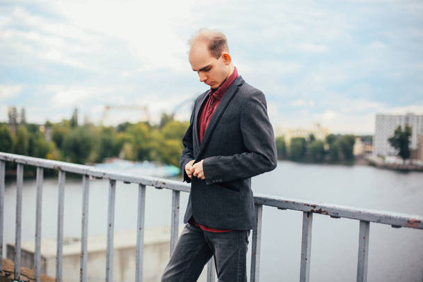 portrait de jeune homme debout sur le pont et posant, nuageux et froid temps venteux gros plan, essaie de boutonner costume
 - Photo, image