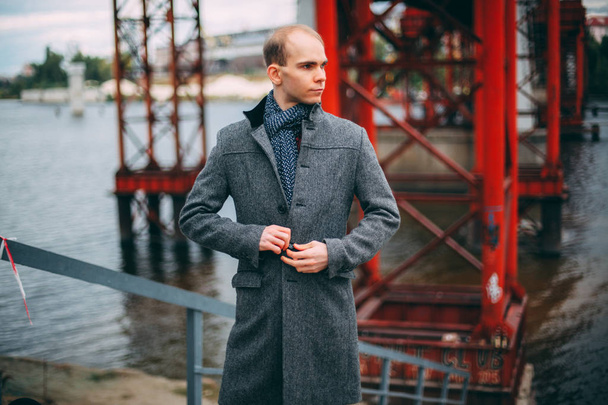young businessman standing on the background of the bridge and coat buttons, serious look successful. cold windy weather closeup - Fotó, kép