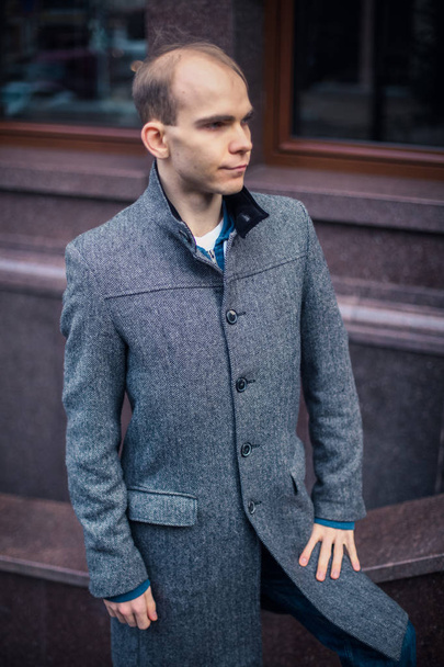 portrait of young man standing near the business center and posing, cloudy and cold windy weather, posing like fashion model successful and bald, big city capital - Φωτογραφία, εικόνα