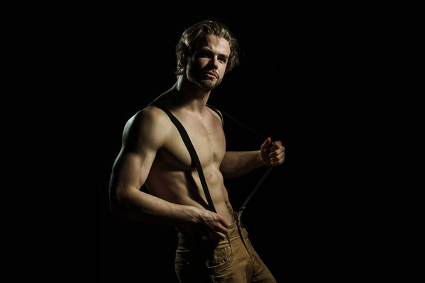 Sexy man is played with his suspenders for trousers on a black background. Seductive fashionable and sensual man - Foto, Bild