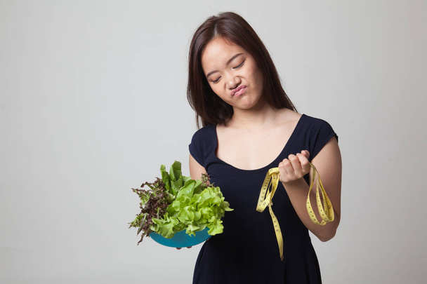 Unhappy Asian woman with measuring tape and salad. - Φωτογραφία, εικόνα