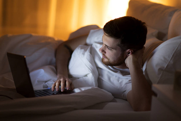 young man with laptop in bed at home bedroom - Foto, imagen