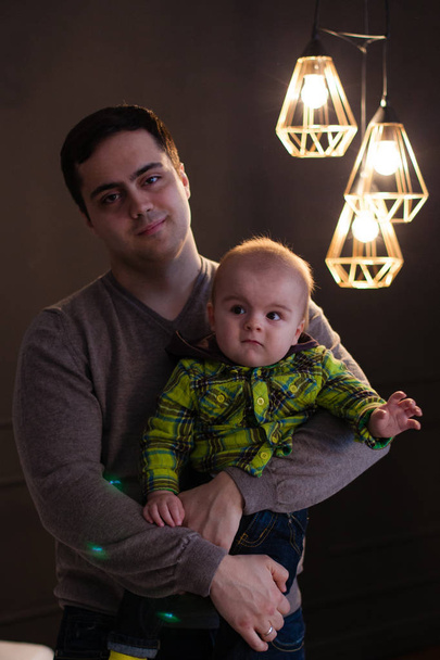 Отец обнимает своего сына рядом с лампой в виде лампочек, сдержанный, знаменитый
 - Фото, изображение