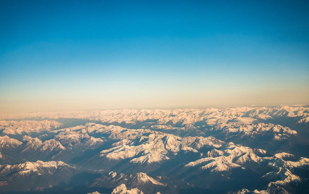 Mirando a través del avión ventana durante el vuelo una nieve cubrió los Alpes italianos y Osterreich con cielo azul sin nubes
. - Foto, Imagen