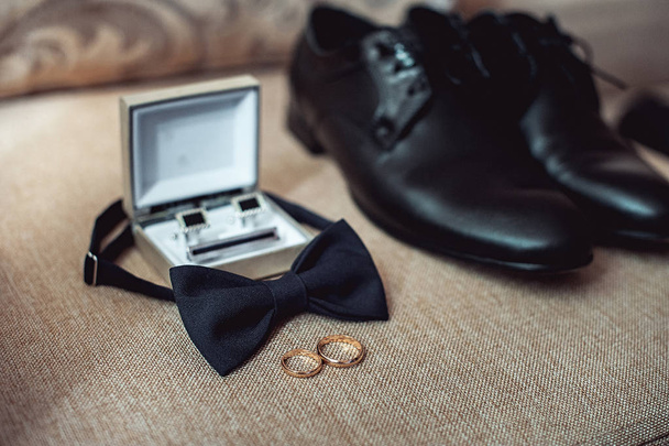 Primer plano de los accesorios de hombre moderno. anillos de boda, corbata negra, zapatos de cuero, cinturón y gemelos
 - Foto, imagen