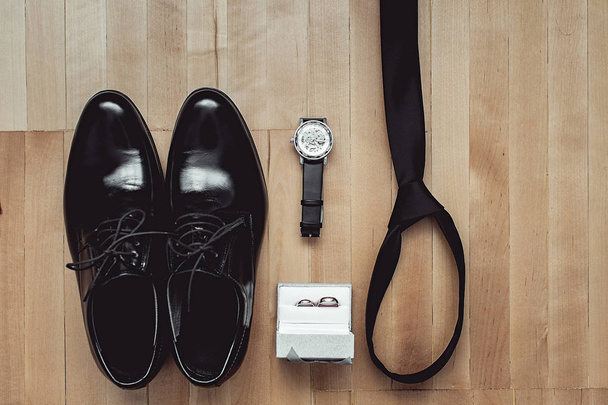 Close up of modern groom accessories. wedding rings, black necktie, leather shoes and watch - Photo, Image