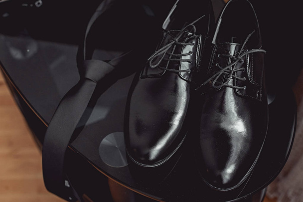 Κοντινό πλάνο, αξεσουάρ, ο σύγχρονος άνθρωπος. μαύρη γραβάτα και δερμάτινα παπούτσια στο τραπέζι μαύρο γυαλί - Φωτογραφία, εικόνα