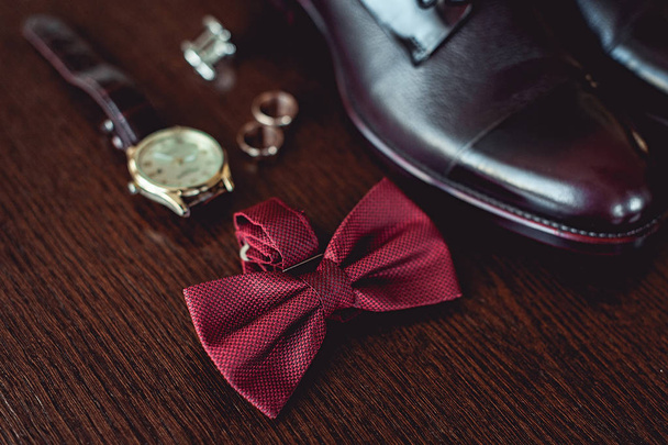 Close up van de moderne mens accessoires. trouwringen, cherry bowtie, lederen schoenen, horloge en manchetknopen - Foto, afbeelding