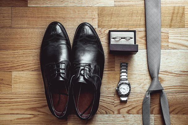 Close up of modern groom accessories. wedding rings, gray necktie, leather shoes and watch - Foto, afbeelding