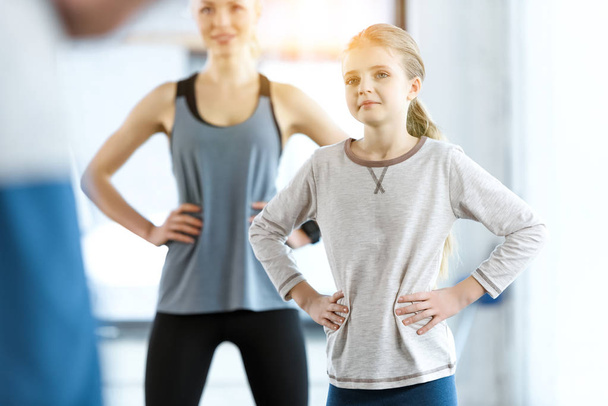 Νεαρή γυναίκα και χαριτωμένο κορίτσι άσκηση με προπονητή στο γυμναστήριο - Φωτογραφία, εικόνα