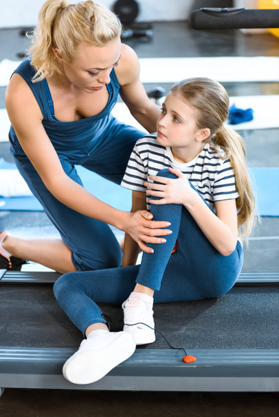 Woman helping girl injured knee sitting on treadmill - Valokuva, kuva