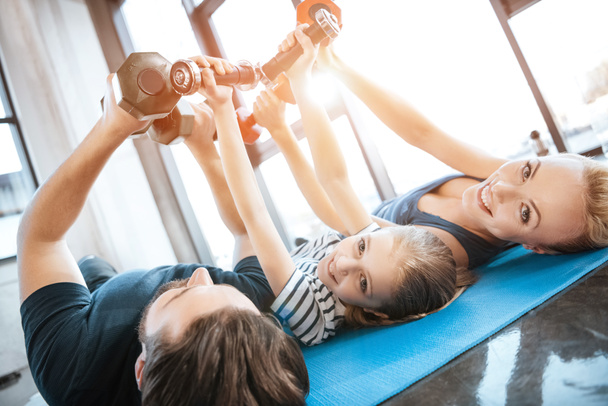 Familia feliz haciendo ejercicio con pesas en el gimnasio, pesas en forma de corazón
 - Foto, Imagen