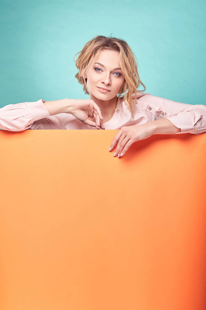Young cute blonde woman looking romantic in studio with turquoise background and orange sheet - Fotoğraf, Görsel