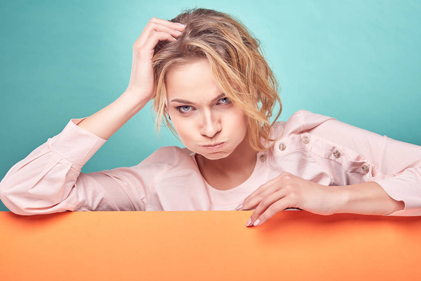 Closeup portrait of young pretty blonde woman with funny face in studio with turquoise background and orange sheet - Foto, afbeelding