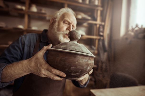 Senior potter in schort keramische kom op workshop onderzoeken - Foto, afbeelding