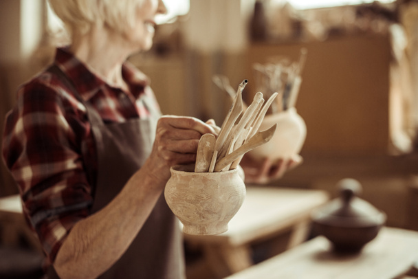 Femme âgée tenant des bols avec des outils de poterie à l'atelier
 - Photo, image