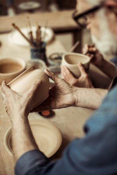 Close up van senior potter in schort en brillen keramische kom te onderzoeken - Foto, afbeelding