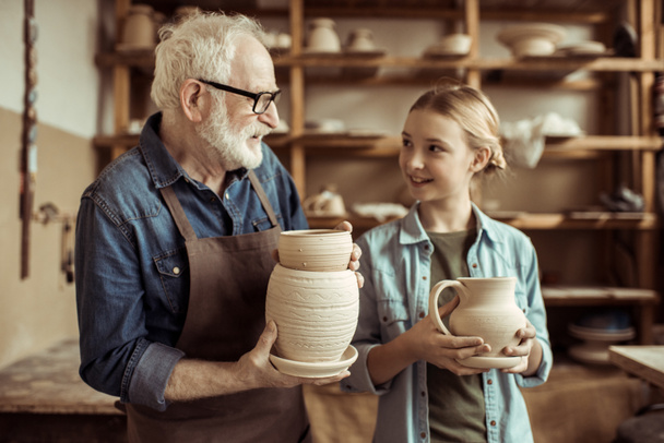 Petite-fille et grand-père tenant et examinant des marchandises en argile
 - Photo, image