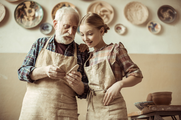 Frontansicht eines älteren Töpfers, der seiner Enkelin Details zeigt, während er in der Werkstatt steht - Foto, Bild