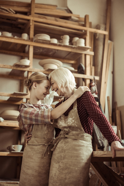Kleindochter knuffelen haar oma terwijl ze permanent in schorten tijdens workshop - Foto, afbeelding